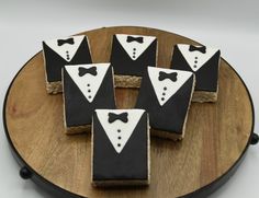 four decorated cookies with black and white tuxedos on them sitting on a wooden platter