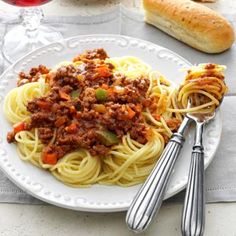 a white plate topped with pasta covered in sauce and meat next to two silver spoons