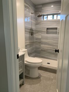 a white toilet sitting inside of a bathroom next to a walk in shower stall under a window