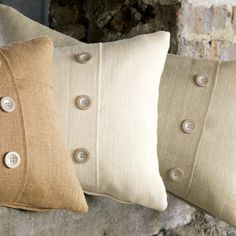 three pillows with buttons on them sitting next to each other in front of a stone wall