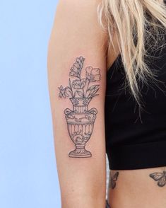 a woman with a tattoo on her arm holding a vase filled with flowers and butterflies