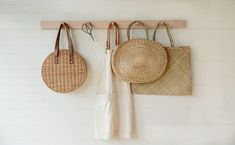 three baskets hanging on a wall with hooks and two purses attached to the wall