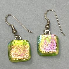 two square shaped earrings with colored glitters on them, one is green and the other is pink