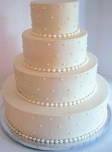 a three tiered white wedding cake with pearls