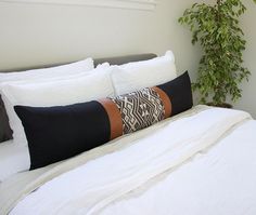 a bed with white linens and pillows on top of it next to a potted plant