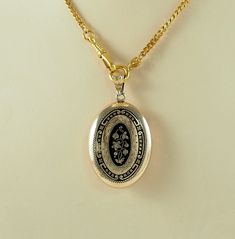 A charming antique Victorian oval gold filled and black enamel sentimental or mourning locket back pendant, in a yellow gold tone. The front with a bleeding heart flower in full bloom with two further buds and foliage, in gilt on a black ground, with a border of scrolls and tiny flower heads.  With an opening machine engraved panel to the reverse with space within for hair or a keepsake, with both frames and one glass. Unmarked. The chain is for display only. Germany 1880s.  8g The opening panel Antique Etched Locket Necklace For Memorial, Antique Oval Jewelry With Black Enamel, Antique Oval Black Enamel Jewelry, Antique Gold Victorian Locket Jewelry, Victorian Yellow Gold Pendant Locket Necklace, Victorian Style Etched Yellow Gold Jewelry, Heirloom Black Enamel Jewelry As Gift, Heirloom Black Enamel Jewelry For Gift, Antique Gold Oval Link Jewelry