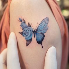 a woman's shoulder with a blue butterfly and rose tattoo on her left shoulder