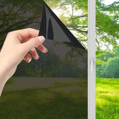 a hand holding a black kite in front of a green field with trees and grass