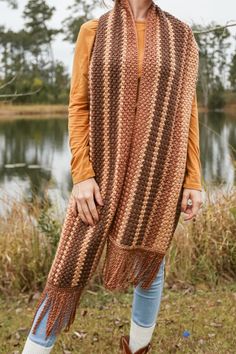 a woman standing in front of a lake wearing a scarf