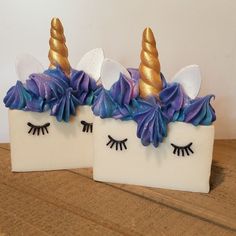 two ceramic unicorns with purple and gold hair on them sitting on a wooden table