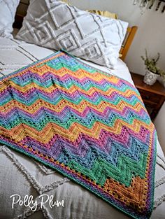 a colorful crocheted blanket on top of a bed next to pillows and a night stand