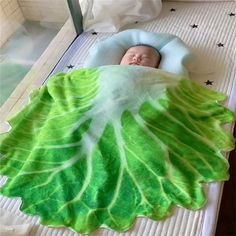 a baby is sleeping in a bed with a green leaf blanket on top of it