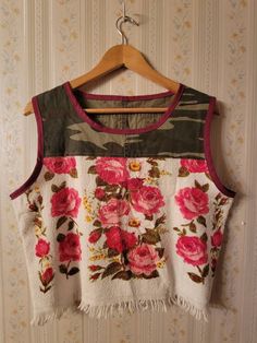 a white top with pink flowers on it hanging from a wall next to a wooden hanger