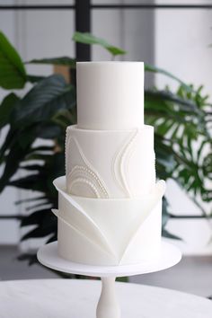 a three tiered white cake sitting on top of a table next to a potted plant