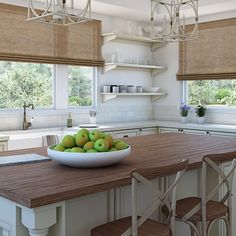 a bowl of green apples sitting on top of a wooden table in a white kitchen