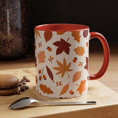 an orange and white coffee mug sitting on top of a wooden table next to a spoon