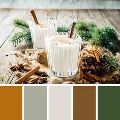 two glasses filled with milk sitting on top of a wooden table next to pine cones and cinnamon