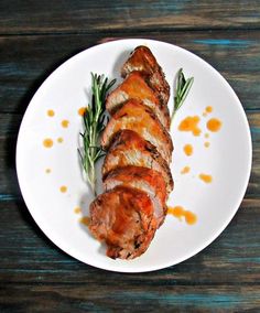 a white plate topped with meat covered in sauce and garnished with green herbs