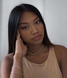 a woman wearing a tan tank top holding her hand to her ear and looking at the camera