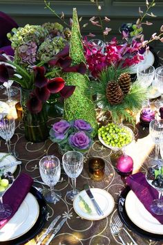 the table is set with plates, silverware and purple flowers in glass vases