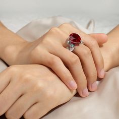 a close up of a person's hand holding a ring with a red stone