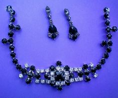 This fabulous glitzy demi is a deep black stone piece accented with clear rhinestones that form a lovely center piece to the necklace, which is accented in the pierced dangle earrings.   The center of the necklace, which consists of a square stone, surrounded by smaller round black and clear stones, is stationary and 2½ inches in length.  The black crystal single strand necklace extends up the piece to the clasp for a total length of 15 inches but it can be worn shorter if so desired.   The pierced dangle earrings are 1¼ inch drop. These pieces are in excellent condition and are from a recent estate sale.  Please view my shop often as I continually add new and interesting items. Thanks for looking and visiting my shop. Square Stone, Clear Stone, Deep Black, Black Stone, Black Crystals, Strand Necklace, Clear Rhinestones, Crystal Necklace, Dangle Earrings