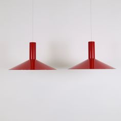 two red lamps hanging from the ceiling in front of a white wall with no one on it