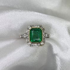 This stunning ring showcases an approx 2.26-carat emerald-cut natural emerald at its center, with a bezel set in 18k yellow gold. A halo of old European cut diamonds surrounds the emerald. Each shoulder of the ring features a pear-shaped diamond, and three additional diamonds on each side of the shank, adding up to a total diamond weight of around approx 0.40 carats. The ring is handcrafted in platinum.  The dimensions of the ring, including the diamond halo, are approximately 12.73mm x 10.87mm. Exquisite Emerald Cut Platinum Emerald Ring, White Gold Emerald Ring With Baguette Cut, Exquisite Green Emerald Platinum Ring, Luxury Green Asscher Cut Diamond Ring, Green Octagon Platinum Ring, Luxury Green Radiant Cut Rings, Octagon Emerald Ring In Platinum, Fine Jewelry, Octagon Emerald Ring In Platinum, Luxury Green Octagon Rings