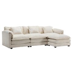 a white sectional couch with pillows on it's back and foot rests against the wall