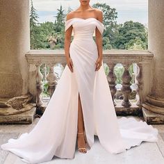 a woman standing in front of a window wearing a white dress with thigh high slits