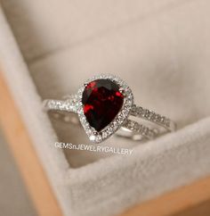 a close up of a ring in a box with a red heart shaped stone on it