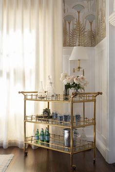 a gold bar cart with vases and cups on it in front of a window