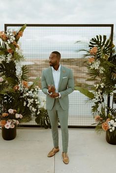 a man in a green suit standing next to flowers and greenery on the ground