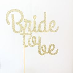 a cake topper that says bride to be on a wooden stick in front of a white wall