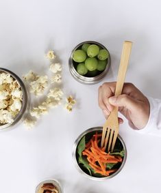 a person is holding a wooden spoon over some food in small metal bowls on a white table