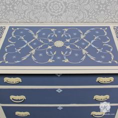 a blue and white chest with gold trimmings on the top, in front of a wallpapered background