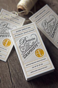 three white and yellow business cards sitting on top of a wooden table next to a spool of thread