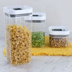 three containers with food in them sitting on a yellow towel next to two jars filled with rice and beans