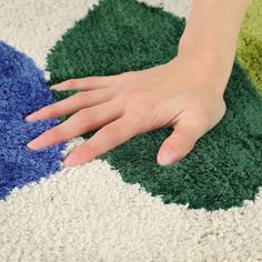 a person's hand on a rug that is colored green, blue and white