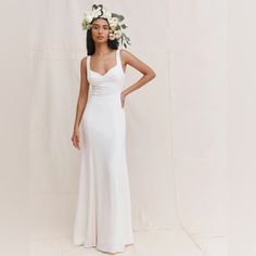 a woman wearing a white wedding dress with flowers in her hair standing against a backdrop