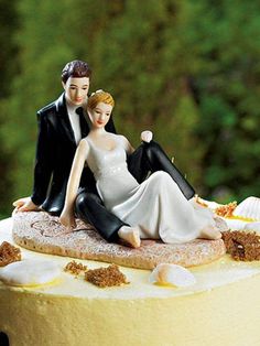 a wedding cake with a bride and groom figurine on top, sitting on a beach