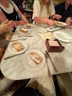 several people sitting at a table with plates of cake on it and silverware in front of them