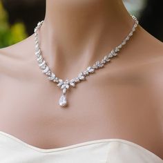 a woman wearing a necklace and earrings on her neck, with flowers in the background