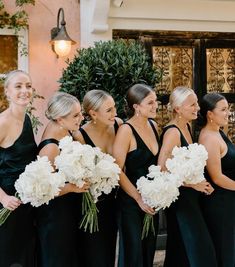 a group of women standing next to each other holding bouquets in front of a building