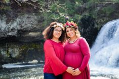 two pregnant women standing in front of a waterfall