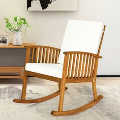 a wooden rocking chair sitting on top of a rug next to a table with a potted plant