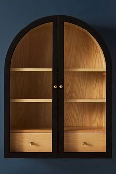 an arched wooden cabinet with glass doors on the front and bottom, against a blue wall