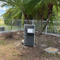 an old fashioned pay phone in front of a white picket fence and palm trees on the other side