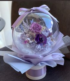 a glass ball with flowers in it sitting on top of a table next to a purple ribbon