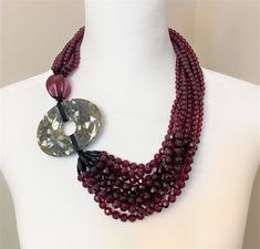 the necklace is adorned with three strands of red beads and a large stone disc pendant